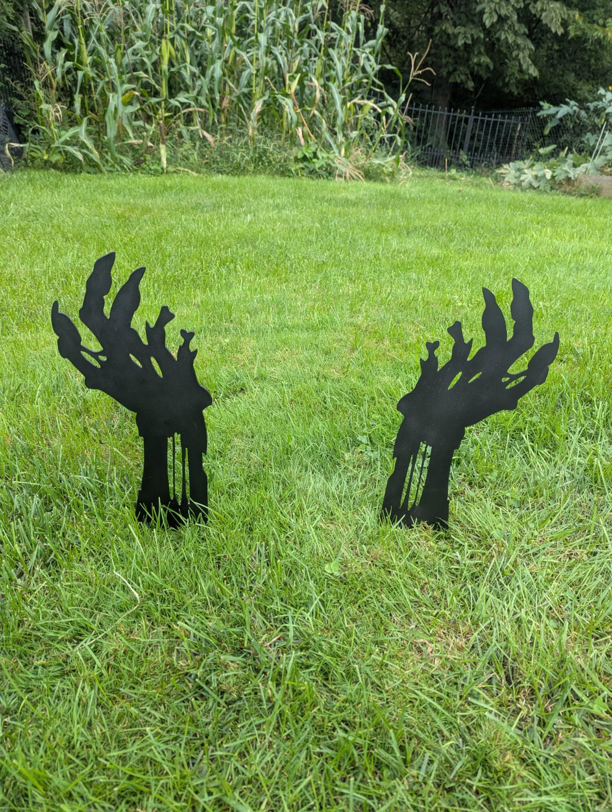 Two black metal zombie hand yard stakes standing in a lawn